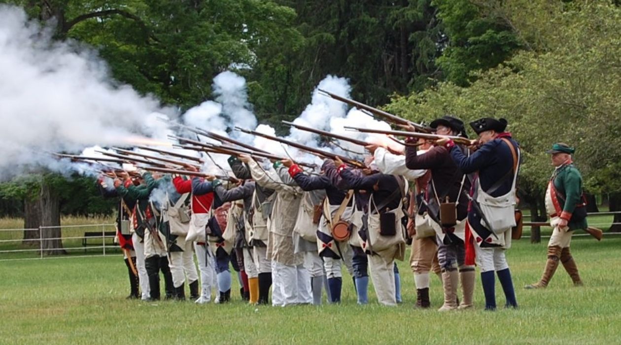 A line of Revolutionary War reenactors fires their weapons during RevCon 2024 at the Franklin D. Roosevelt Presidential Library and Musem in Hyde Park on June 8, 2024 